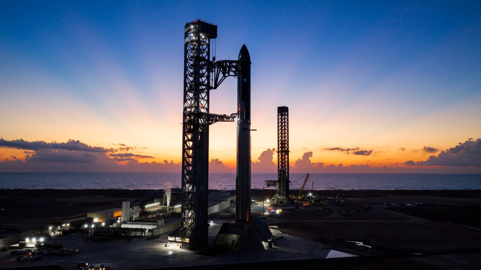 Starbase's launch towers and the Flight 14 Starship stack at sunrise, with the Gulf behind them