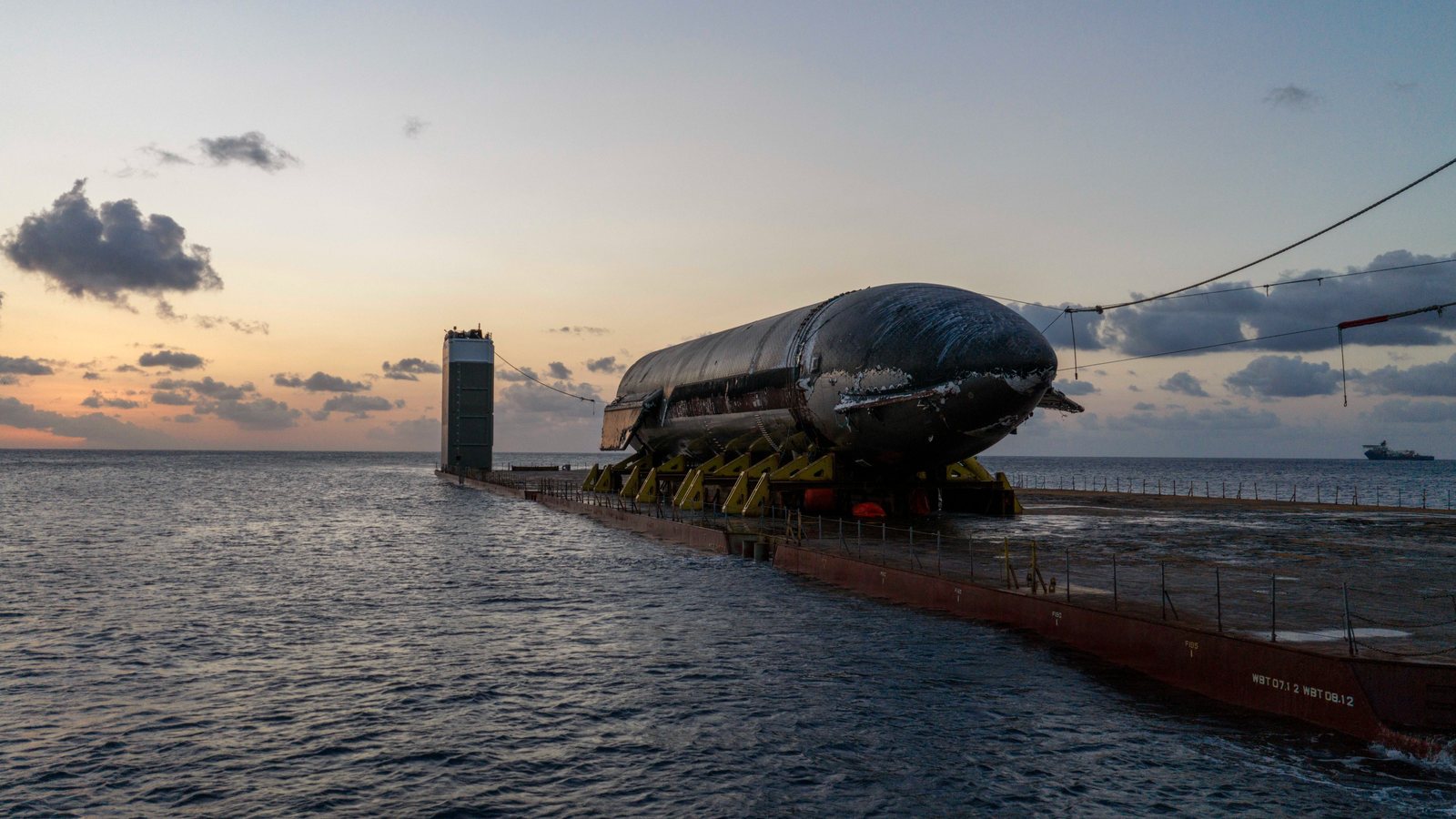 Starship Ship 40 strapped onto yellow cradles on the deck of the heavy-lift ship Forte at dusk