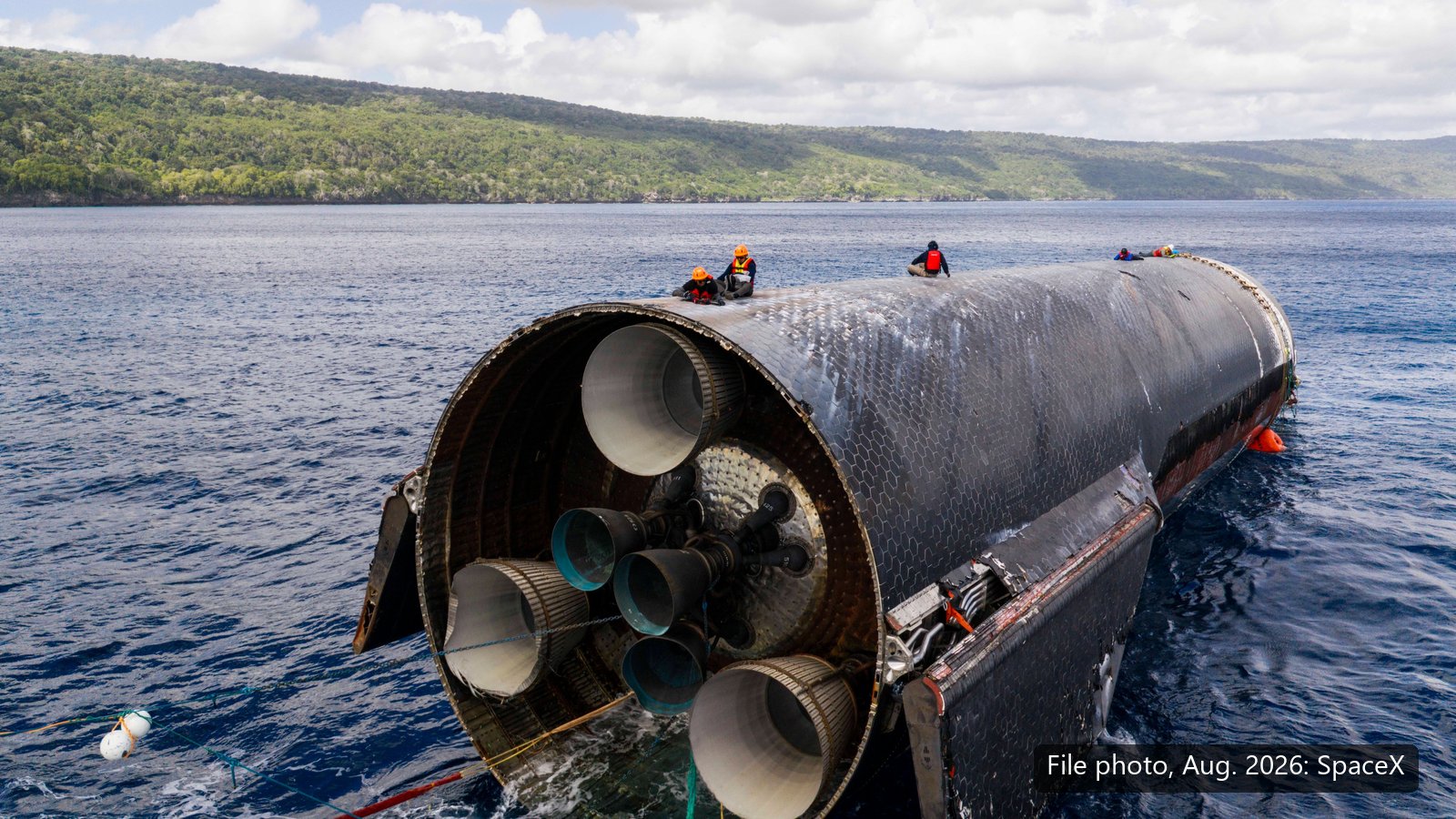 Ship 40 floating on its side in blue water off Christmas Island, its engines facing the camera, with recovery crew sitting on top