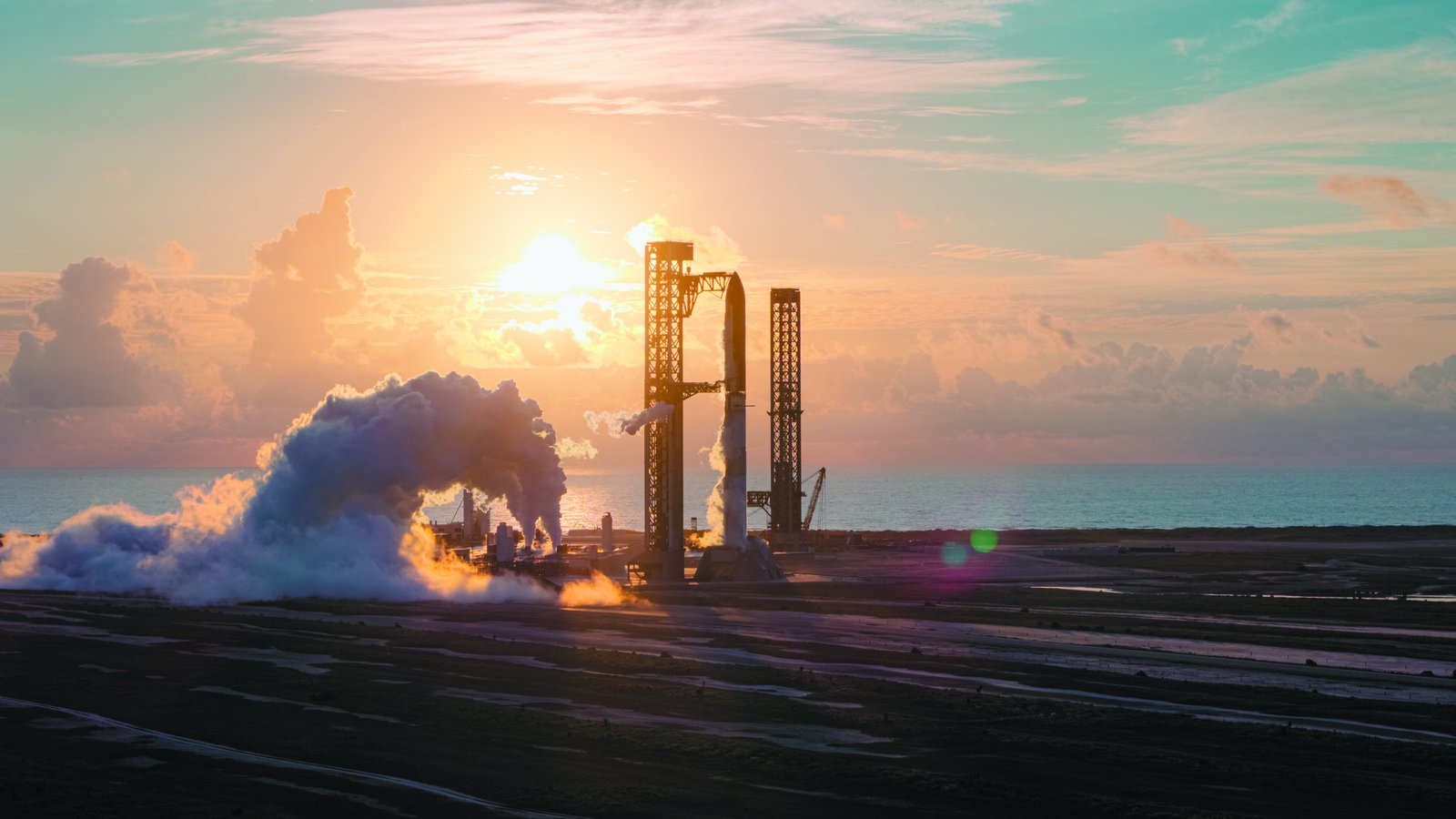 Vapor rolls across the Starbase launch site at sunrise as the Flight 14 stack stands in the launch tower, with the Gulf behind it