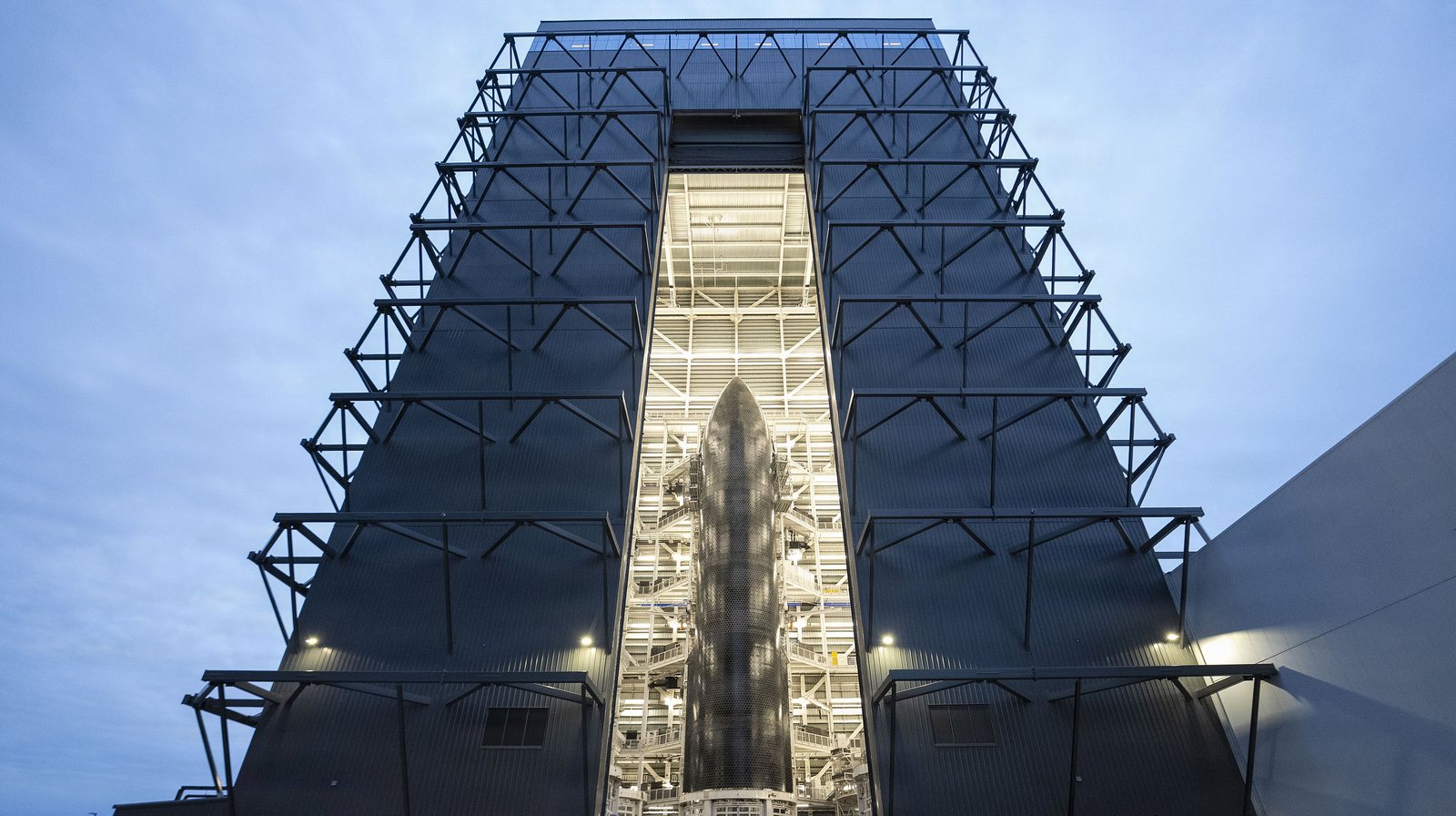 Starship Ship 39 stands inside the lit, open door of Megabay 2, a tall dark steel production building at Starbase, at dusk
